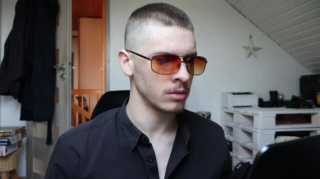 Young serious man with buzz cut and orange sunglasses looking at laptop, cyber hacker concept, generation Z technology portrait