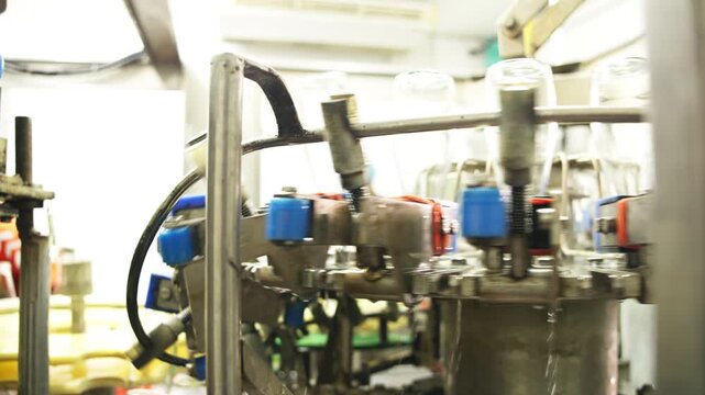 Close-up of industrial bottling equipment precisely filling glass containers with liquid during high-speed beverage production process in factory