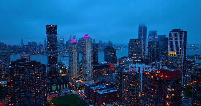Flight over the thriving urban city with street lights on. Jersey City, New Jersey, USA under the thick cloudscape at dusk time.
