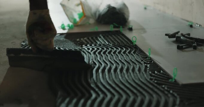 Applying tile adhesive with notched trowel on floor during tile installation close up