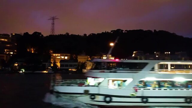 Night View of Illuminated Waterfront Mansions and Luxury Houses on the Bosphorus Coast with a Passenger Ferry Passing in Istanbul, Turkey