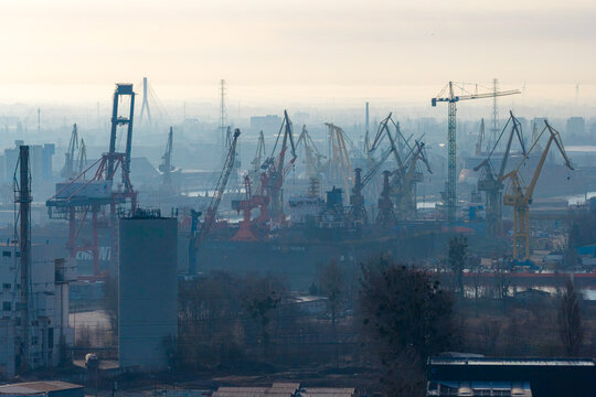Gdansk, Poland - 28 March 2026: Aerial view of the industrial shipyard with numerous cranes, cargo ships, and a cable-stayed bridge in the hazy background.