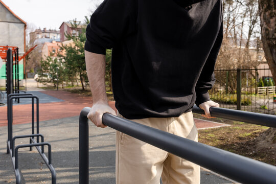 A man doing strength training on parallel bars at an outdoor sports ground
