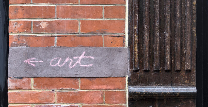 art sign with arrow drawn in chalk on a red brick building in new york city pointing to gallery museum public exhibit exhibition cursive letters drawing