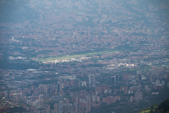 An expansive aerial view of the Jos&eacute; Mar&iacute;a C&oacute;rdova International Airport (MDE) serving Medell&iacute;n, Colombia. The photograph showcases the unique circular terminal design, a long asphalt runway, and seve