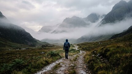 Fototapeta premium Hiker walking solitary mountain trail amidst low clouds