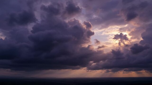 Towering dark purple and golden storm clouds loom across a dramatic sky over the sea during sunset, creating a moody atmospheric scene.