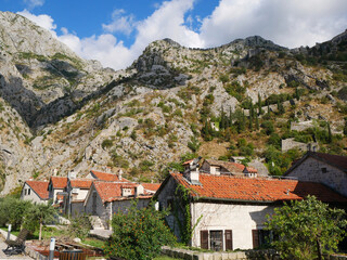 Fototapeta premium Kotor Old Town Stone Houses with Red Rooftops and Ancient Fortress Walls on Rocky Mountain, Montenegro