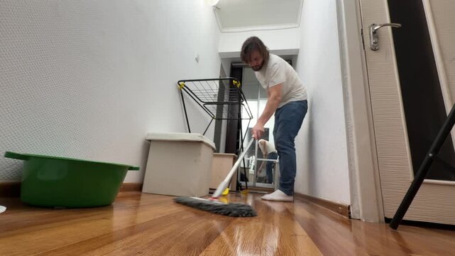 Man washing wooden floor with mop at home, cleaning apartment interior, wet floor cleaning routine, household chores