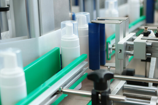 Production of cosmetics and skin care products. White plastic bottle is moving along conveyor belt. Labeling machine. Bottle has no label. Conveyor belt is in production.
