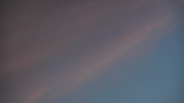Time-lapse of streaky orange and blue clouds flowing through an evening sky creating a dramatic shifting sunset atmosphere with vibrant color motion