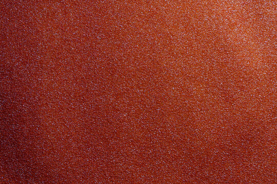 Red abrasive sandpaper texture macro background, closeup. Macro shot of red sandpaper surface with abrasive grains. Concept of woodworking metal finishing construction tools and DIY home renovation