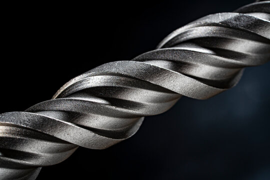 Macro steel spiral drill bit texture on dark background. Metal drill bit spiral flutes on black background. Concept of industrial tools engineering precision construction and hardware equipment