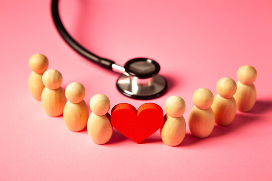Stethoscope and wooden people with red heart on pink background.