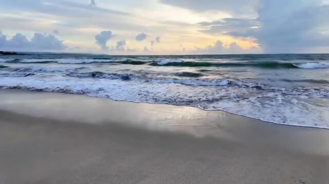 Beautiful evening beach footage from Kuta Beach Bali showing ocean waves, sandy shoreline, dramatic clouds, sunset atmosphere, distant tourists and relaxing tropical travel scenery with natural ambien