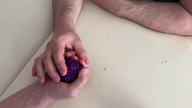 Close-up of elderly person doing hand rehabilitation with a therapist using a massage ball. Concept of physiotherapy, recovery, healthcare, aging population, and assisted care.