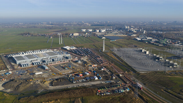 Groningen, Netherlands - 20 January 2026: Aerial view of Datacenter Westpoort with its cooling units, an adjacent electrical substation, and surrounding green fields under a clear blue sky.