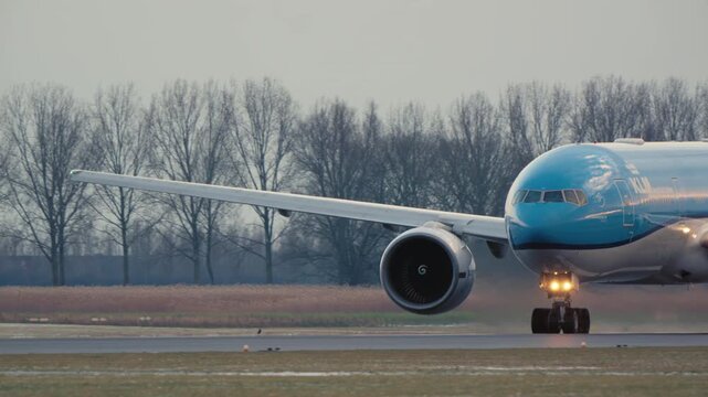 AMSTERDAM, NETHERLANDS - JANUARY 5, 2026: KLM Boeing 777 widebody taxiing to runway at Amsterdam Airport Schiphol at winter dusk, bare trees in background, landing light on