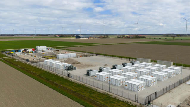 Dronten, Netherlands - 04 April 2026: Aerial view of the Olsterdwarspad battery energy storage system facility with rows of white containers and wind turbines in the background.