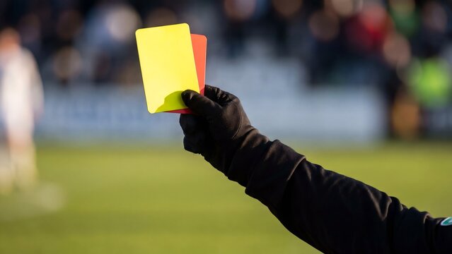 Referee hand holding yellow and red cards on football pitch, soccer discipline rules concept with blurred match background