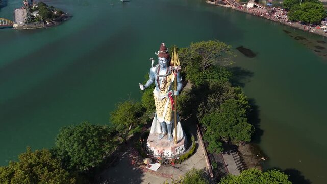 Orbit drone footage captures the iconic Lord Shiva statue located in Swami Vivekanand Park on the banks of the sacred Ganges River in Haridwar, Uttarakhand, India.