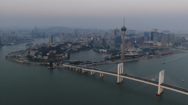 Macao - 18 February 2026: Aerial view of the Macau Tower and Sai Van Bridge spanning the water with the city skyline under a hazy sky.