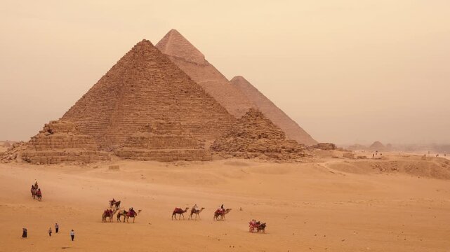 Tourists walking and riding camels in desert valley with Giza pyramids. A cinematic view of desert valley near Giza plateau, with tourists exploring on foot, riding camels, and in horse-drawn carriage