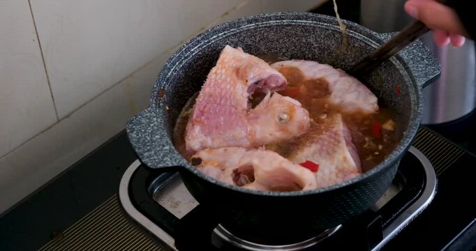 Vietnamese red fish cooking in gray pan with chili garlic and salt simmering on gas stove showing traditional soup preparation step by step