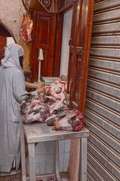 Counter with sheep and goat heads and other primal cuts right on the street, in the Medina, where a local woman is about to buy. Marrakesh-Morocco-319