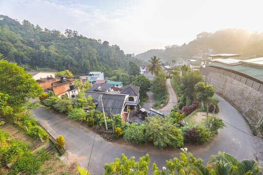 Panoramic high-angle view of a serene hillside village nestled in lush green mountains under soft morning sunlight, showcasing a peaceful tropical landscape. Kandy town in Sri Lanka.