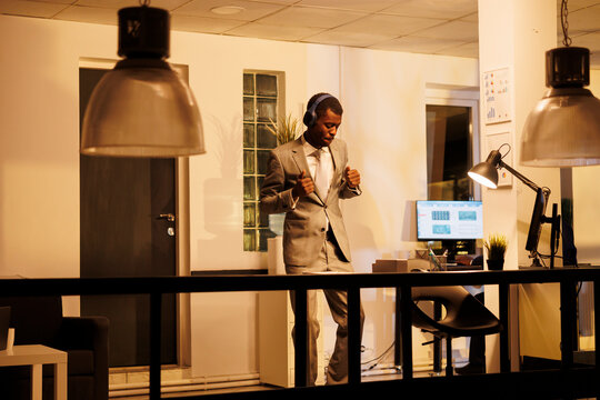 Businessman wearing headphones showing dance moves in startup office during work break. Executive manager dacing and having fun after finishing company strategy, planning investment plan