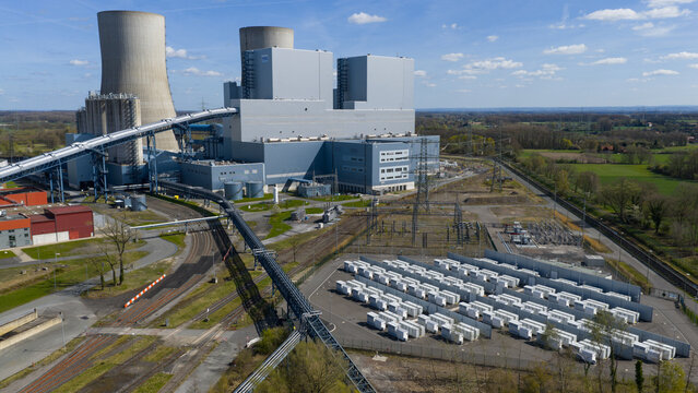 Hamm, Germany - 06 April 2026: Aerial view of RWE Westfalen power plant with its massive cooling towers, industrial buildings, and a large battery storage facility under a clear blue sky.