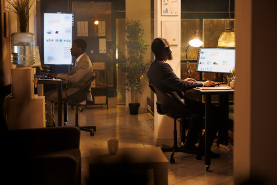 Businessman wearing headpones listening music in startup office, analyzing financial graph report, planning investment strategy to help increase company proft. Manager working late at night