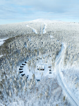 Sirkka, Finland - 05 April 2026: Aerial view of OloResort Levi Lapland with modern black cabins nestled in a snow-covered pine forest under a bright winter sky.