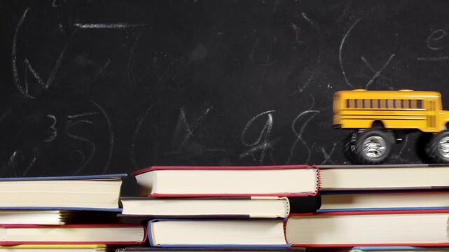 Toy yellow schoolbus driving over school books in front of chalkboard. Classic American public school bus traveling quickly over school textbook indicating excitement at going back to school.