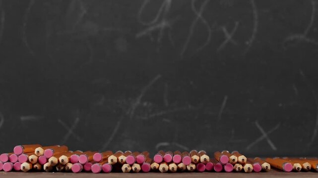 Toy yellow schoolbus driving over school pencils in front of chalkboard. Classic American public school bus traveling quickly over school supplies indicating excitement at going back to school.