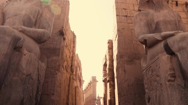 Exit view of Luxor Temple with pharaonic statues. Smooth Steadicam shot moving backward through Luxor Temple, revealing large seated pharaonic statues and inscriptions on the walls