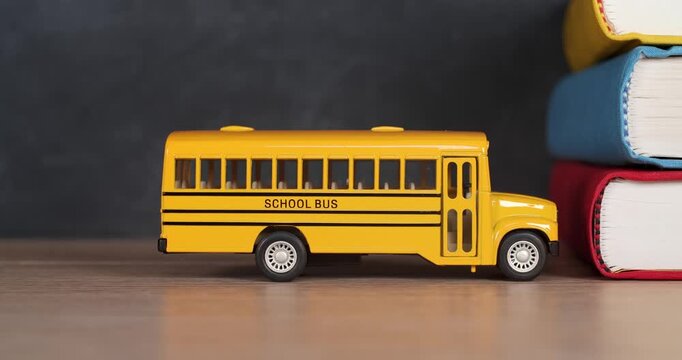 Toy yellow schoolbus driving into school books in front of chalkboard. Classic American public school bus traveling quickly towards school textbooks indicating excitement at going back to school.