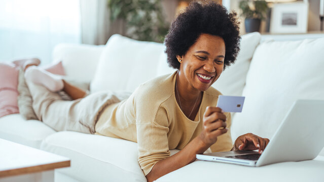 Smiling Woman Shopping Online With Credit Card and Laptop While Relaxing on a Home Couch