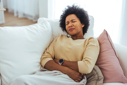 Woman With Stomach Pain Resting On Couch At Home Looking Uncomfortable