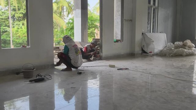 Two construction workers repairing a lower wall foundation &mdash; one with a hand grinder, the other using a chisel and hammer on site.
