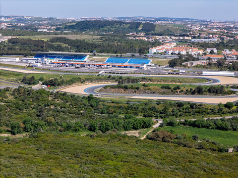 Alcabideche, Portugal - 03 April 2026: Aerial view of Autodromo Fernanda Pires da Silva race track with its blue grandstands and winding asphalt curves surrounded by green hills and urban buildings.