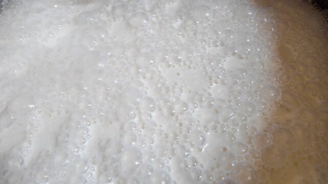 Close-up push-in on milk bubbles in aluminum pot with temperature probe visible. Dairy processing, food quality control and macro texture concept.