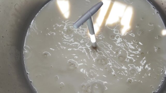 Close-up of fresh farm milk being poured from ladle into aluminum separator bowl. Homemade dairy processing, organic food and farm production concept.