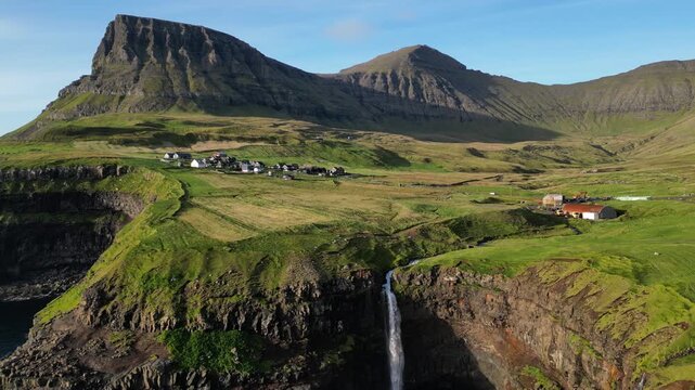 Cinematic 4K aerial drone shot soaring over the rugged cliffs of Gasadalur and Mulafossur waterfall