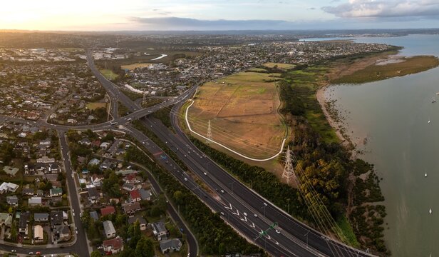 Aerial view of Auckland, New Zealand, showing the convergence of residential areas, a major highway with traffic, and the coastline.  Te Atatu South, Auckland, NZ