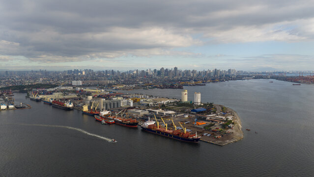 Manila, Philippines - 01 March 2026: Aerial view of Manila Multipurpose Terminal with large cargo ships docked at the pier and the city skyline under a cloudy sky.