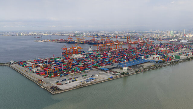 Manila, Philippines - 01 March 2026: Aerial view of Manila Multipurpose Terminal with rows of colorful shipping containers and orange cranes under a hazy sky.