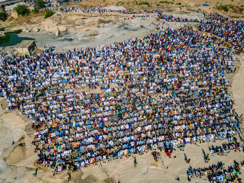 Zaria, Nigeria - 28 October 2025: Aerial view of a large crowd of people gathered for prayer at the Jum'at Mosque, Hayin Dogo Palladan, on a rocky landscape under bright sunlight.