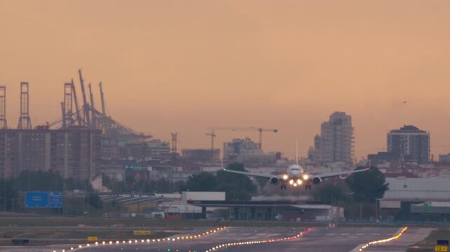 VALENCIA, SPAIN - JANUARY 23, 2026: A commercial jet makes its final approach and lands on a runway at sunrise. Head-on shot shows touchdown and braking with a city skyline and port cranes in the